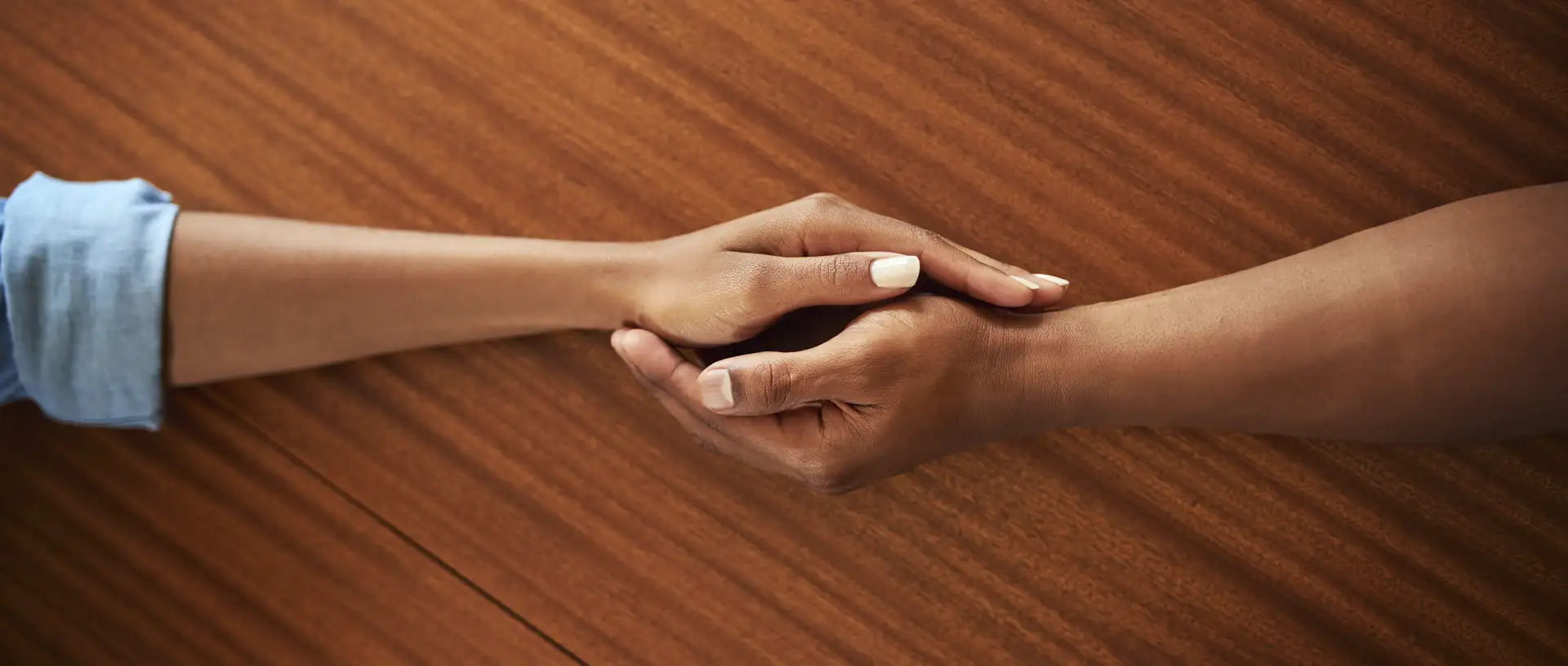 terapiaadulto_martinezpicon Primer plano de dos manos entrelazadas sobre una mesa de madera, representando apoyo y acompañamiento emocional.